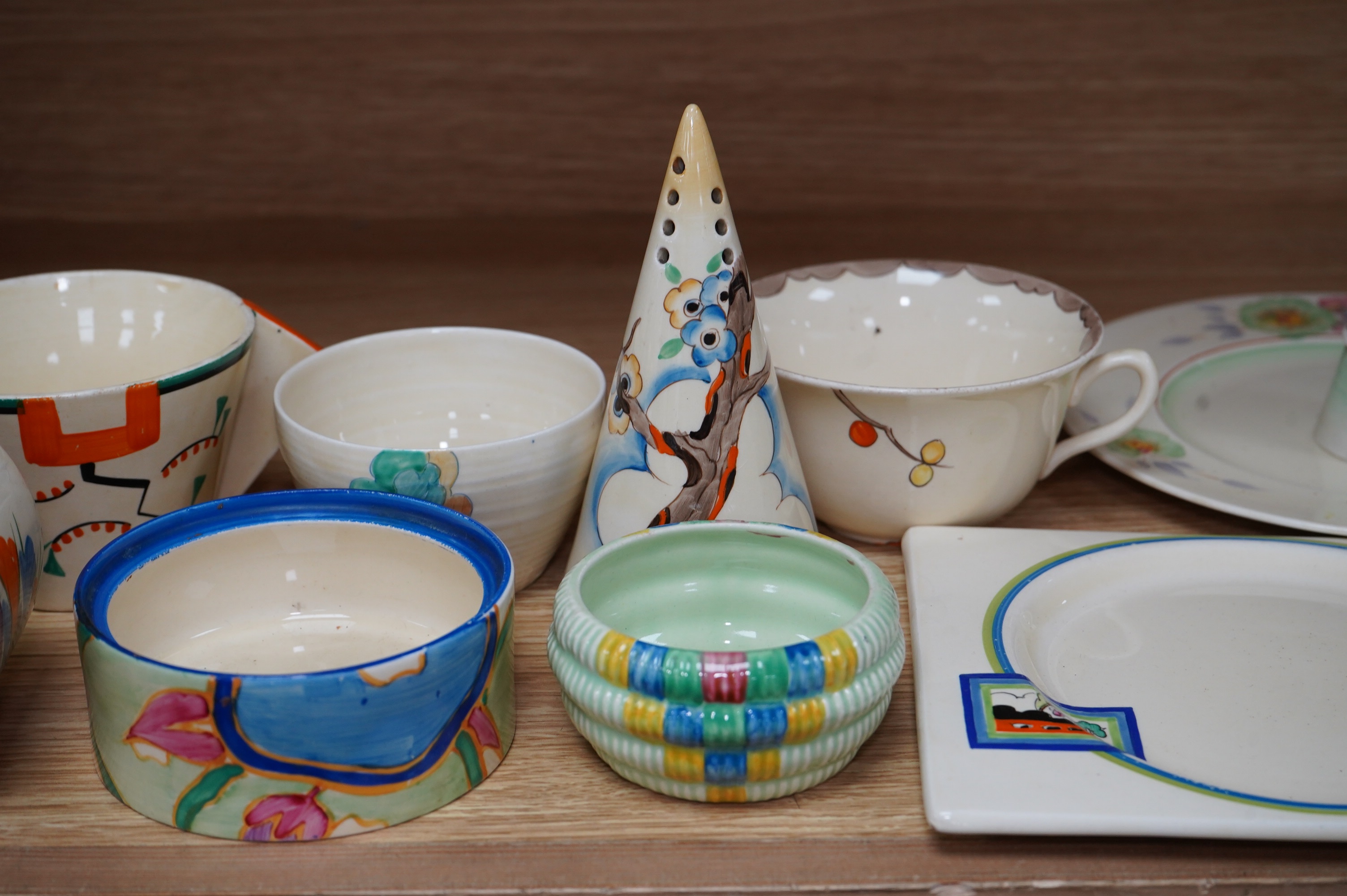 A collection of Clarice Cliff including; a Tiger Tree conical sugar sifter (c.1937), a cup marked 5799, a two handled pomegranate cup, a bowl, two plates, a mustard pot, etc. Condition - fair